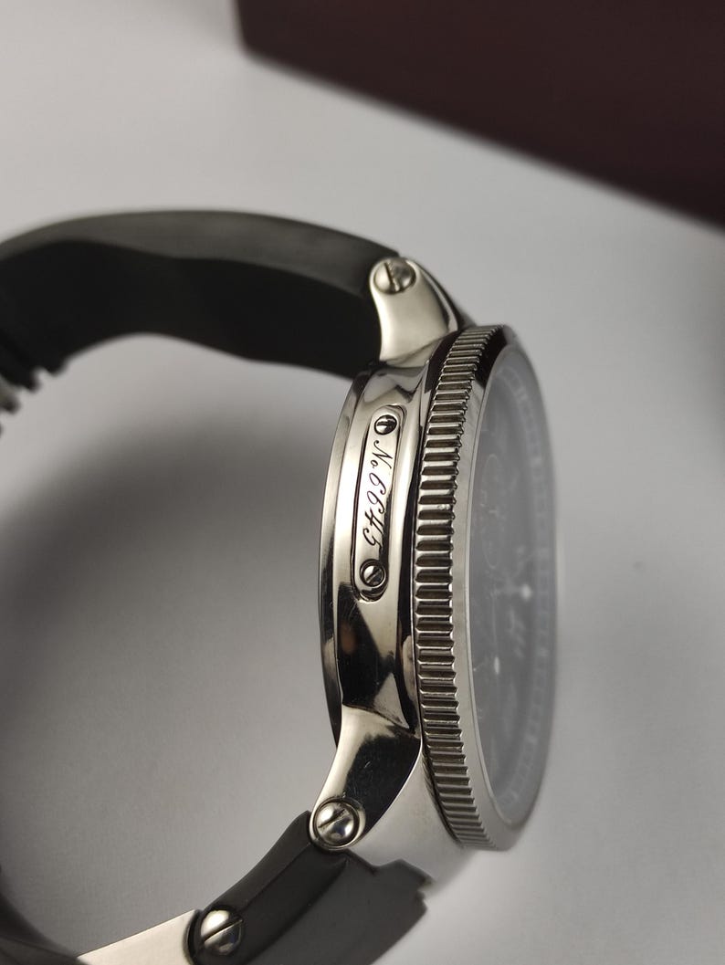 Puede incluir: Primer plano de un reloj de pulsera plateado con esfera negra y correa de caucho negra. El reloj tiene un bisel texturizado y el texto "NCC43" es visible en el lateral.