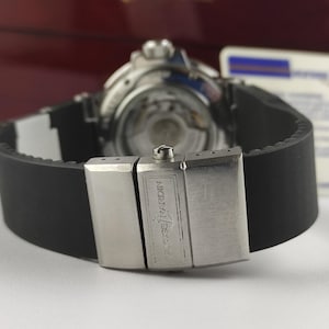 K&ouml;nnte beinhalten: Nahaufnahme einer Luxus-Armbanduhr mit schwarzem Kautschukarmband und silberner Schlie&szlig;e. Das Uhrwerk ist sichtbar. Die Schlie&szlig;e ist mit dem Markennamen "Ulysse Nardin" graviert.
