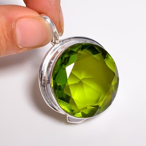 May include: A round, faceted, lime-green gemstone pendant set in a polished silver-toned metal bezel. The circular stone features a brilliant cut with multiple triangular facets that reflect light, secured by a simple silver-toned metal bail.