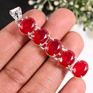 May include: A silver pendant featuring five oval-cut, vibrant red stones arranged in a vertical line. The stones are set in polished silver prongs, connected by small silver links, and topped with a triangular silver bail for attachment to a chain.