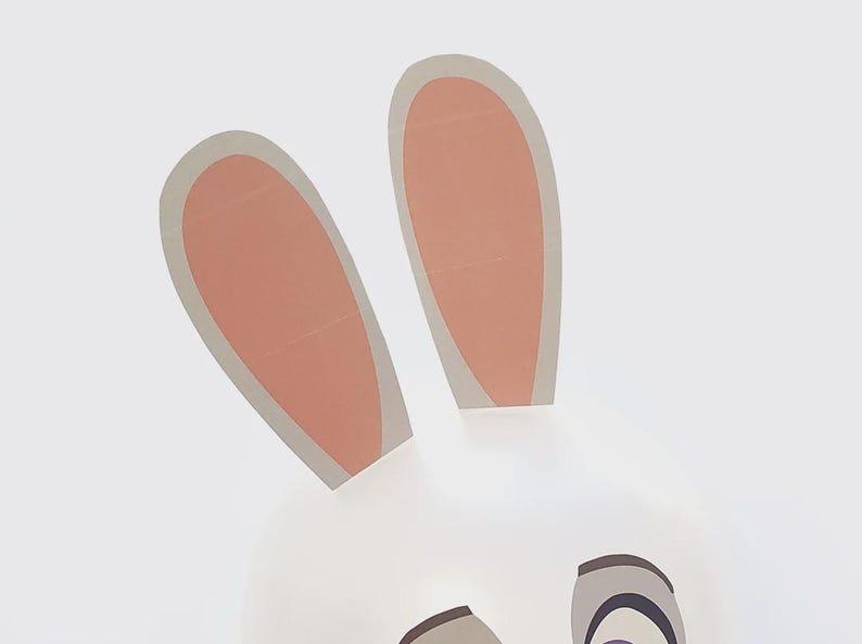 May include: A whimsical illustration of a bunny face with two upright ears. The ears are light pink inside with a gray border, and the face is white. The eyes are gray and black.