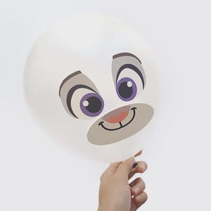 May include: A white balloon with a cartoon face printed on it. The face has large eyes with purple irises, gray eyebrows, and a smiling mouth. The balloon is held by a hand against a white background.