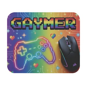 Op de afbeelding: Een regenboogkleurige muismat met het woord "GAYMER" in gepixelde regenboogletters. Een gepixelde controller-afbeelding staat op de mat, samen met een zwarte gamingmuis met regenboog LED-accenten.