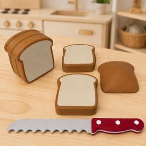 May include: A toy set consisting of a brown and beige loaf of bread, two individual slices of bread, and a serrated toy knife with a red handle featuring three white dots. The bread pieces have a smooth, rounded shape and a light-colored center.