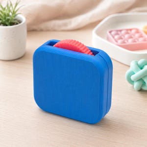 May include: A vibrant blue, rectangular fidget toy with a textured finish. A red, ridged roller is visible within the opening. The toy is designed for sensory play and stress relief.