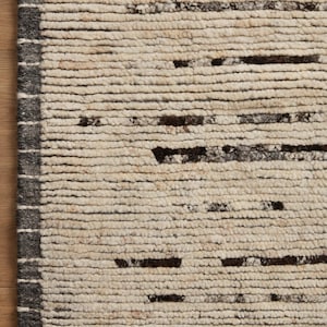 May include: A rectangular area rug featuring a thick, cream-colored, high-pile texture with horizontal rows of dark brown and charcoal gray dashes. A solid dark charcoal gray border runs along the left edge, accented by thin, vertical white lines.