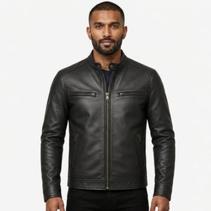 Puede incluir: Chaqueta de cuero negra con cremallera, dos bolsillos en el pecho y cuello alzado. La chaqueta la lleva una persona y es de estilo clásico.