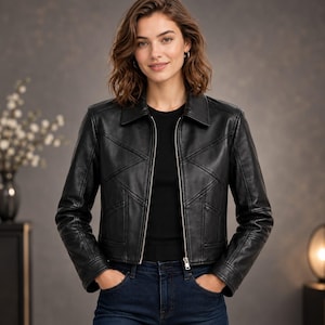 May include: A black leather jacket featuring a structured collar, long sleeves, and a central silver-toned zip closure. The jacket is constructed with multiple stitched panels creating geometric patterns across the front and shoulders.