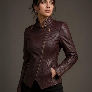 May include: A deep burgundy leather jacket featuring an asymmetrical gold-tone zipper closure, a high stand-up collar with snap buttons, quilted shoulder and side panel detailing, and zippered pockets on the front and sleeves.