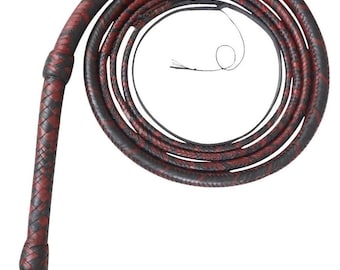 Op de afbeelding: Een lange, opgerolde zweep met een gevlochten patroon van donkerbruine en dieprode leren strengen. Het handvat is verstevigd met een knoop en de basis bevat een klein zwart leren lipje met een in reliëf gedrukte letter R en een polsband.