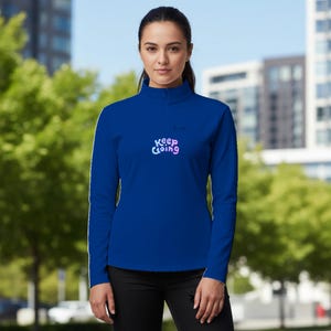 Könnte beinhalten: Ein königsblaues Langarmshirt mit Stehkragen und dem Schriftzug "Keep Going" in einem Farbverlauf aus Pink und Blau. Das Shirt hat weiße Streifen an den Ärmeln.