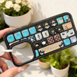 May include: Black phone case designed to resemble a keyboard, featuring blue and black keys with cat illustrations. The case has a curved design and a white loop for holding. The text "Luck Black Cat" is visible.