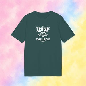 Puede incluir: Una camiseta de manga corta de color verde azulado oscuro con un estampado gráfico blanco en el pecho. El diseño muestra un cubo de líneas con un cerebro dentro, acompañado del texto blanco THINK OUT OF THE BOX en una fuente negrita.