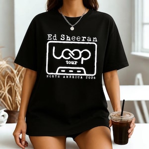 May include: A black short-sleeved t-shirt featuring a white graphic print on the chest. The design includes the text Ed Sheeran, the word Loop, the word tour, and the text North America 2026, all enclosed within a rectangular border.