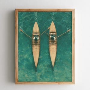 May include: A framed wall art print depicting an aerial view of two wooden rowboats on vibrant teal water. Each boat is occupied by a single rower wearing a dark vest and white shirt, holding oars extended outward. The scene is captured from above.