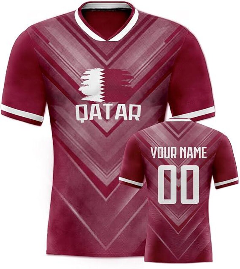 May include: Maroon soccer jersey with white accents. The front features the word "QATAR" below a graphic. The back has the text "YOUR NAME" above the number "00". The jersey has a V-neck collar and white stripes on the sleeves.