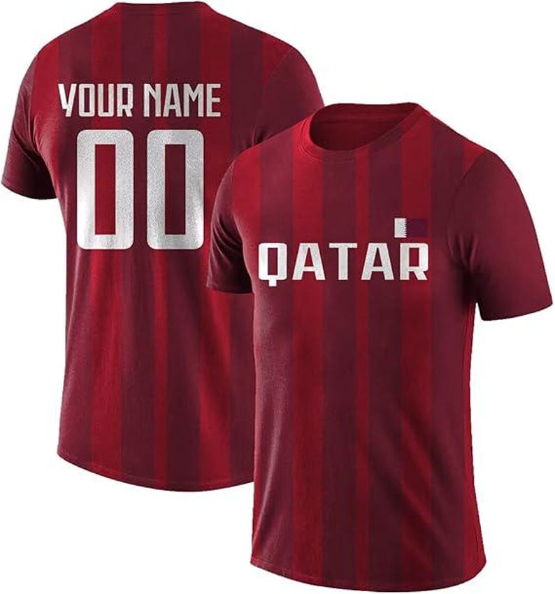 May include: Two maroon t-shirts with vertical stripes. One shirt displays "YOUR NAME" and the number "00" in white. The other shirt has "QATAR" in white, with a small flag graphic. Both shirts have a crew neck.