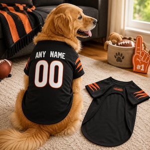 May include: A black pet jersey with orange tiger stripe accents on the sleeves. The back features the text ANY NAME and the number 00 in white with orange outlines. A second identical jersey lies flat nearby with the text CINCINNATI on the chest.