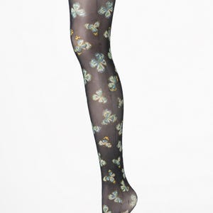 May include: Sheer black tights featuring a repeating pattern of butterflies in shades of blue, yellow, and white. The hosiery has a solid black waistband and a vertical seam running down the back of the leg, extending from the top to the heel.