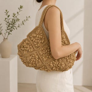 May include: A tan crochet shoulder bag constructed from multiple square panels featuring a raised, textured floral pattern. The bag has a wide, integrated strap and is made from a natural-coloured fibre, showcasing intricate stitching and a soft, slouchy shape.
