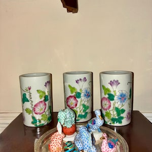 May include: Three white ceramic vases with floral designs of pink, purple, and blue morning glories. A silver tray holds several small, colorful animal figurines, including rabbits, ducks, and elephants. The items are displayed on a dark wooden surface.