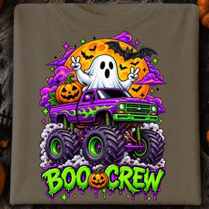 Puede incluir: Una camiseta color topo con un gr&aacute;fico de un fantasma blanco haciendo signos de paz, sentado en un cami&oacute;n monstruo morado con llamas verdes. Hay una luna naranja grande, murci&eacute;lagos, nubes moradas y una calabaza. El texto dice BOO CREW.