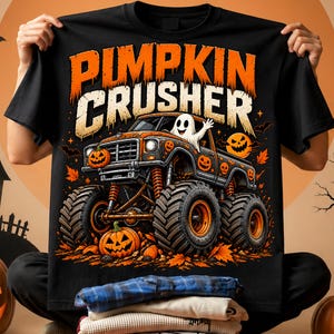 Puede incluir: Una camiseta negra con un gr&aacute;fico de un cami&oacute;n monstruo de neum&aacute;ticos grandes, decorado con calabazas de Halloween naranjas y un fantasma en el asiento del conductor. El texto PUMPKIN CRUSHER aparece en naranja y blanco sobre el cami&oacute;n.