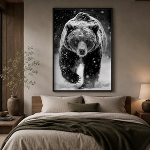 May include: A rectangular wall art print featuring a black and white photograph of a large bear walking through falling snow. The bear is centred, facing forward, with its thick fur covered in light snow, set against a dark, snowy background.