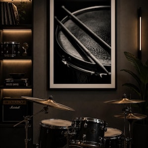 May include: Monochrome framed print of a drum and drumsticks. A drum kit with cymbals is in the foreground. A Marshall amplifier and shelves with books and records are in the background.