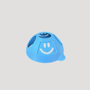 Peut inclure: Une sphère bleu clair imprimée en 3D avec un motif de visage souriant. La sphère comporte plusieurs ouvertures circulaires et une petite protubérance arrondie. Le visage souriant est blanc et est centré sur le devant de la sphère.