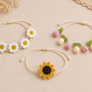 May include: Three handmade crochet bracelets. One features white daisies with yellow centers, another has pink and cream-colored flower buds with green leaves, and the third showcases a yellow sunflower with a brown center. All have adjustable beige cords.