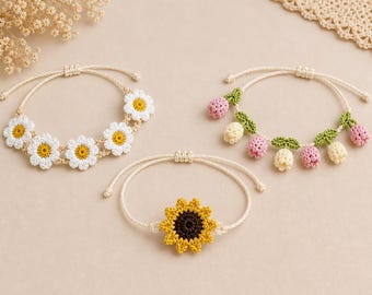 Puede incluir: Tres pulseras hechas a mano con ganchillo. Una presenta margaritas blancas con centros amarillos, otra tiene capullos de flores rosas y crema con hojas verdes, y la tercera muestra un girasol amarillo con un centro marrón. Todas tienen cordones beige ajustables.