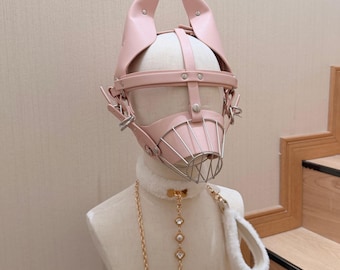 May include: A light pink faux leather headpiece featuring upright pointed ears and a metal wire muzzle cage. The set includes a white faux fur collar with a gold-toned chain leash adorned with three clear crystal-like accents and a white fur handle.
