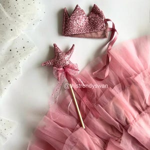 May include: A pink princess-themed set including a sequined crown, a star-shaped wand with a bow, and a tulle skirt. The crown and wand have a glittery finish. The image includes the text "@histrendyswan".