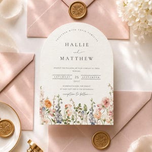 May include: Wedding invitation with floral border and the names Hallie and Matthew. The invitation is arched at the top and includes the date, time, and location of the wedding. Pink envelopes and gold wax seals are also visible.