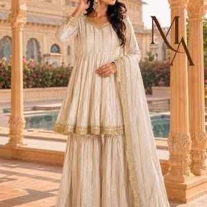 May include: A cream-coloured peplum-style tunic with long sleeves and gold vertical stripes, paired with matching wide-leg flared trousers. The outfit features intricate gold embroidery along the neckline and hem, accompanied by a long, matching dupatta.