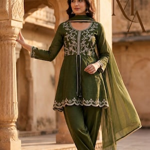 May include: An olive green tunic and trousers set featuring intricate white floral embroidery on the bodice and scalloped hemline. The ensemble includes a matching sheer olive green dupatta with a thin gold border, creating a coordinated look.