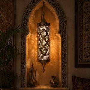 Op de afbeelding: Een decoratieve messing hanglamp met ingewikkelde uitgesneden patronen hangt in een gewelfde nis. De lamp verlicht de ruimte en benadrukt de details van het ontwerp. De nis heeft een plank met een messing kan en vaas.
