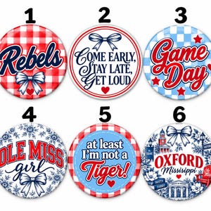 May include: A set of six circular pin-back buttons featuring various designs. Button 1 has a red gingham pattern with the text Rebels. Button 2 says Come Early, Stay Late, Get Loud. Button 3 has a blue checkered pattern with the text Game Day. Button 4 says Ole Miss girl. Button 5 says at least I'm not a Tiger!. Button 6 features Oxford Mississippi with illustrations of local landmarks.