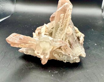 May include: A cluster of quartz crystals with a light brown hue. The crystals are clustered together, with some larger, pointed formations and smaller, more rounded ones. The overall shape is irregular and textured, with a natural, earthy appearance.