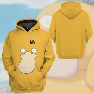 May include: A yellow hooded sweatshirt featuring a graphic of a duck-like face with two round eyes, a large beige bill, and a small black tuft of hair on the forehead. The interior of the hood is dark gray, and the back of the hoodie is plain yellow.