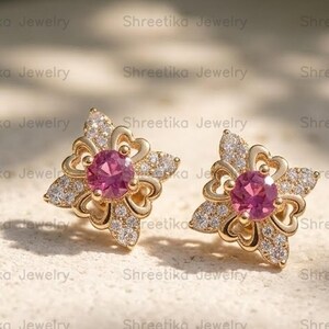 Könnte beinhalten: Ein Paar goldene Ohrstecker mit einem zentralen runden rosa Edelstein, der von einem vierzackigen sternförmigen Rahmen umgeben ist. Der Rahmen ist mit kleinen klaren Pavé-Steinen und filigranen, durchbrochenen Metallverzierungen versehen.