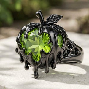 Könnte beinhalten: Ein Ring mit einem facettierten, apfelförmigen Edelstein in Limettengrün, eingefasst in eine schwarze Metallfassung, die an tropfende Flüssigkeit erinnert. Das Design umfasst ein kleines schwarzes Blatt am Stiel und eine glatte, dunkle Ringschiene.