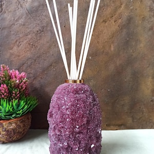 May include: A purple crystal diffuser with white reeds. The diffuser has a gold-coloured band at the top. The crystal-like texture covers the entire body of the diffuser. The reeds are inserted into the top of the diffuser.