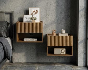 May include: Two wall-mounted wooden nightstands featuring a vertical fluted texture on the drawer fronts. Each unit includes an open storage shelf below the drawer. The left nightstand holds a small framed print and a plant, while the right holds a radio.