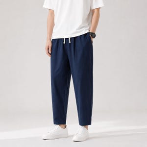 Peut inclure: Un pantalon bleu marine avec une coupe droite et décontractée, une taille élastique dotée d'un cordon de serrage blanc et deux poches latérales. Le pantalon est porté avec un t-shirt blanc à manches courtes et des baskets blanches.