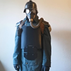May include: A vintage-style gas mask and helmet set. The mask has circular lenses and a corrugated hose. The outfit includes a dark blue coat, chest armor, and shoulder pads. A grenade is attached to the coat.