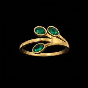 May include: A gold ring with three oval-cut emeralds. The ring has a unique design, with the emeralds set in a leaf-like arrangement. The band is smooth and polished, and the overall look is elegant and sophisticated.