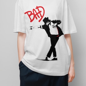 May include: White t-shirt featuring a black and red graphic of a person in a hat and suit, striking a dance pose. The word "BAD" is written in red above the figure.