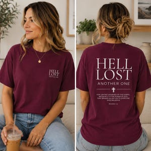 May include: A maroon short-sleeve t-shirt featuring white text. The front displays 'HELL LOST ANOTHER ONE' in small print. The back features the same text in large font, a cross symbol, and the Bible verse Romans 1:16 in white lettering.